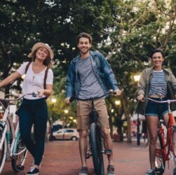 Tres personas pasen en sus bicicletas por una calle arbolada.
