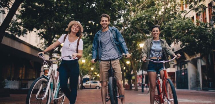 Tres personas pasen en sus bicicletas por una calle arbolada.